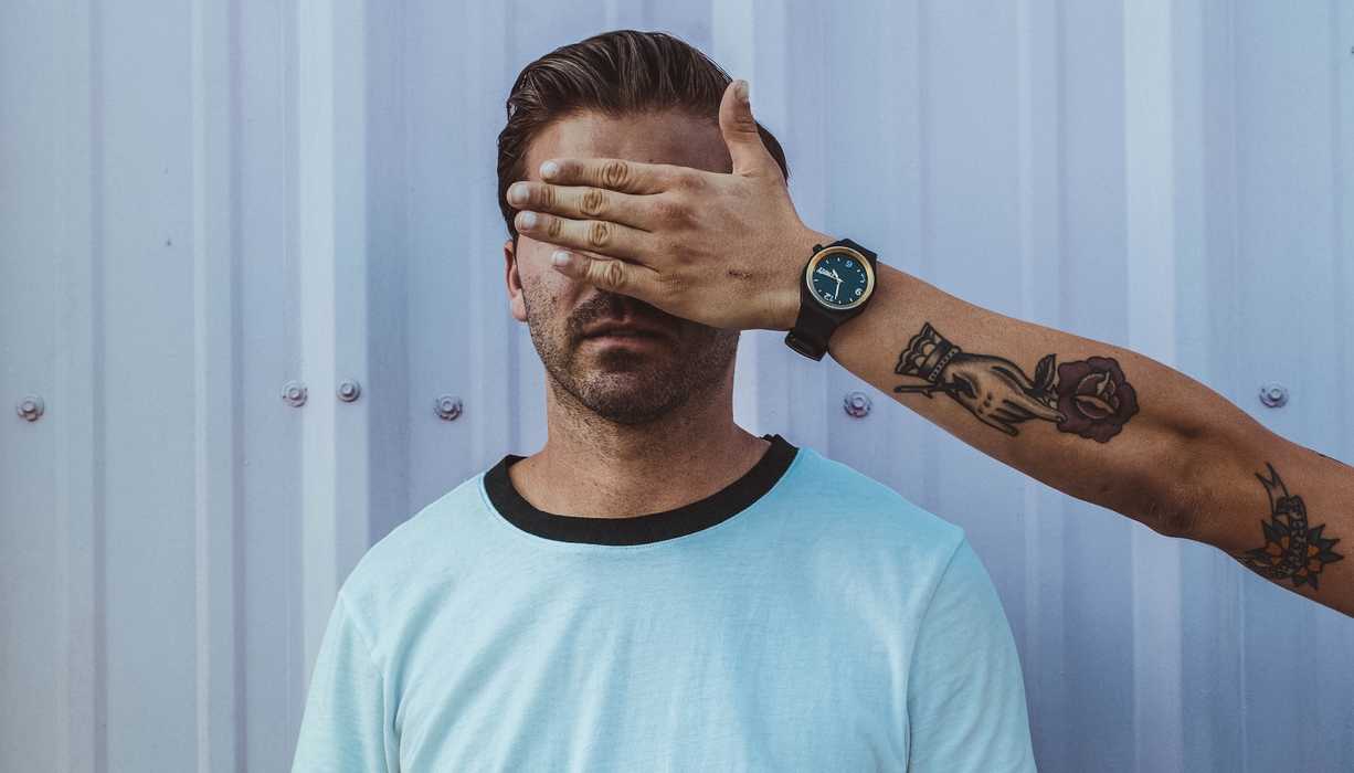 Someone is blocking a man's eyes by holding a hand before his face.