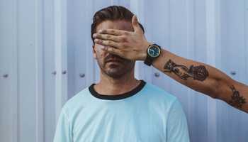 Someone is blocking a man's eyes by holding a hand before his face.